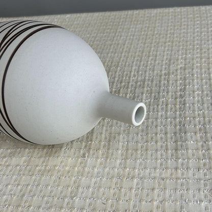 White ceramic vase with black stripes on a textured surface