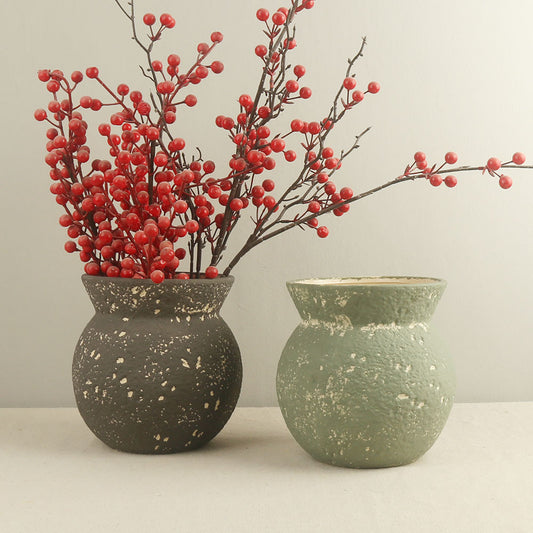 Two ceramic vases with speckled textures, one black and one green, each containing red berries.
