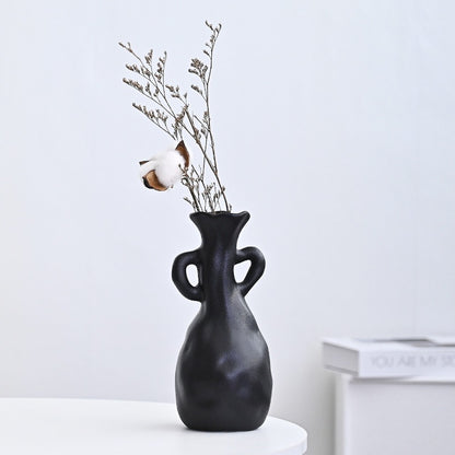 Black vase with dried branches on a white surface against a light gray background