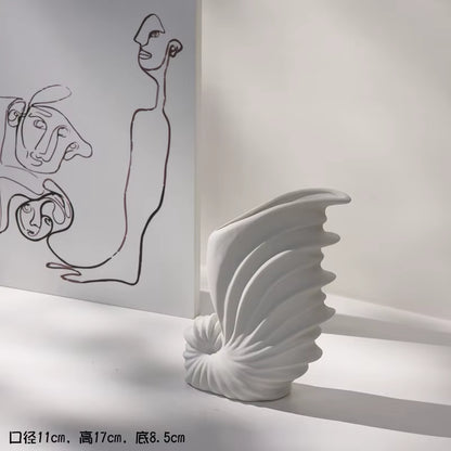 White ceramic vase with shell design on a white surface, with abstract line art in the background.