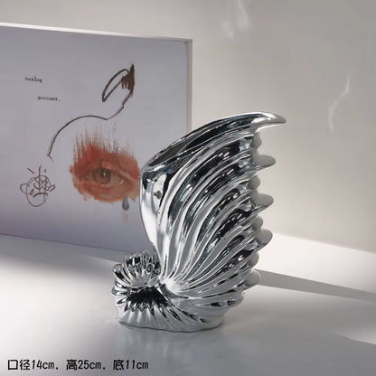 Silver abstract sculpture on a white surface with a blurred artwork in the background