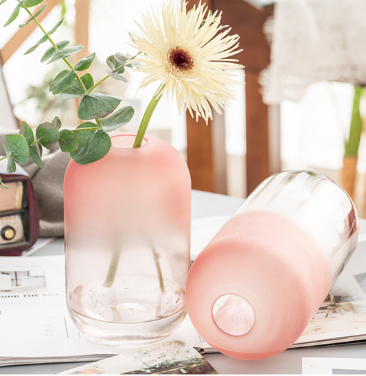 Pink glass vase with a flower and a matching pink electronic device on a surface.