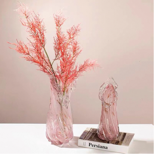 Two glass vases with pink dried branches on a white surface with a book underneath.