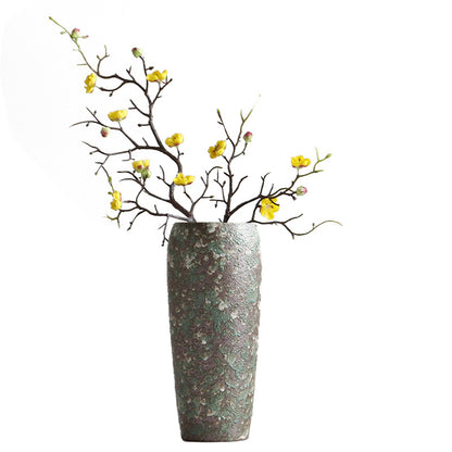 Decorative vase with textured surface holding branches with yellow flowers on a white background