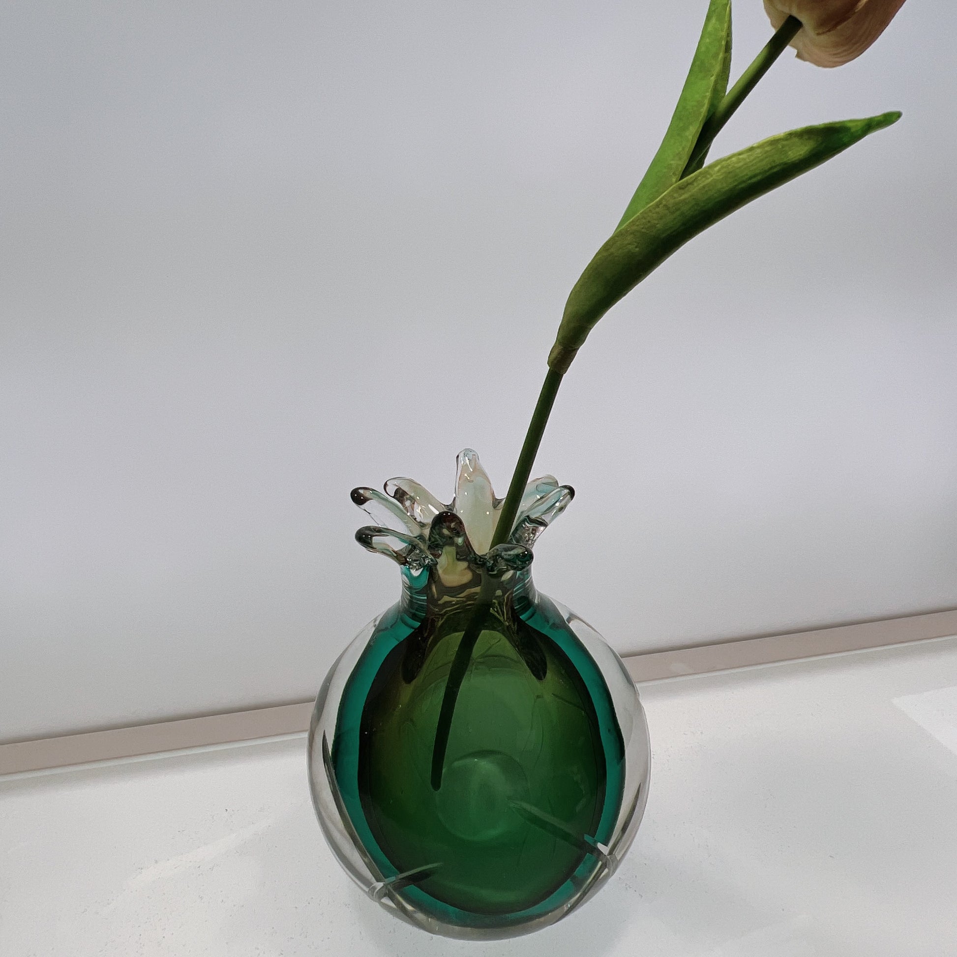 Green glass vase with a single flower on a white surface