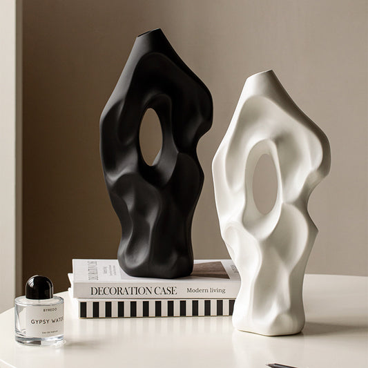Two abstract sculptures, one black and one white, on a surface with books and a perfume bottle.