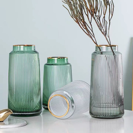 Set of green and gray glass vases with ribbed texture on a light surface.