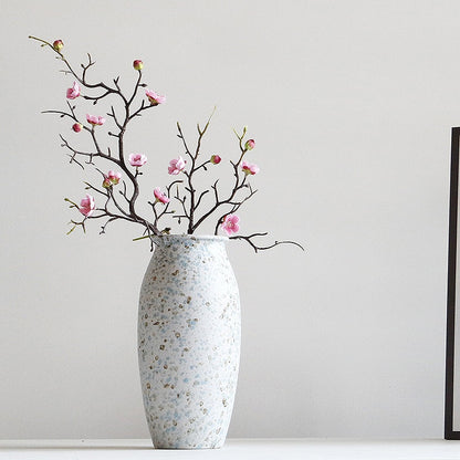Decorative vase with speckled pattern and floral branch against a plain background