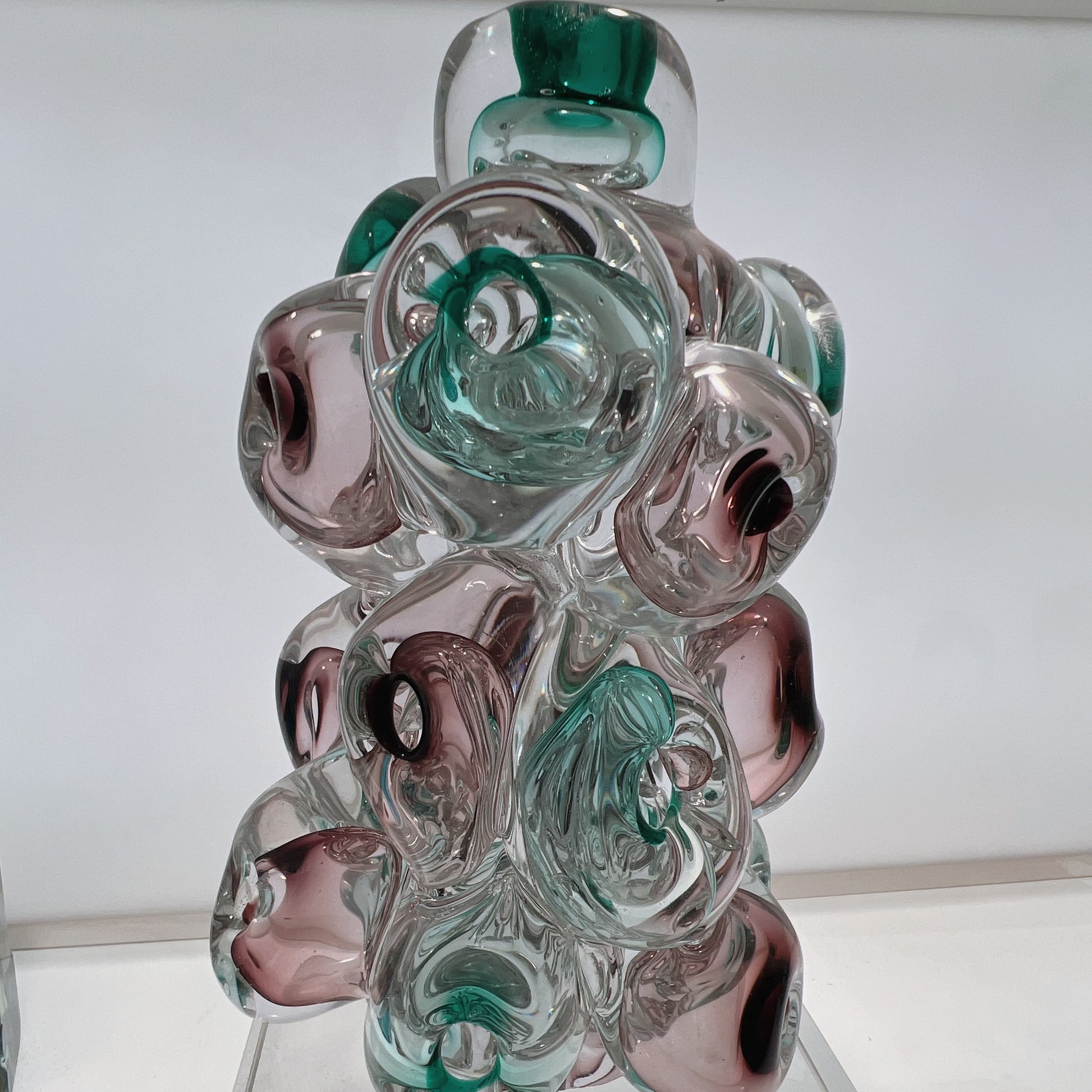 Glass sculpture with swirl patterns in green, clear, and pink on a white background
