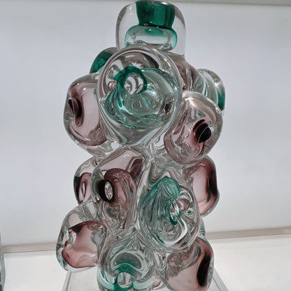 Glass sculpture with swirl patterns in green, clear, and pink on a white background