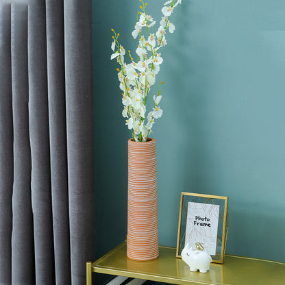 Tall cylindrical vase with white flowers on a green shelf against a teal wall.