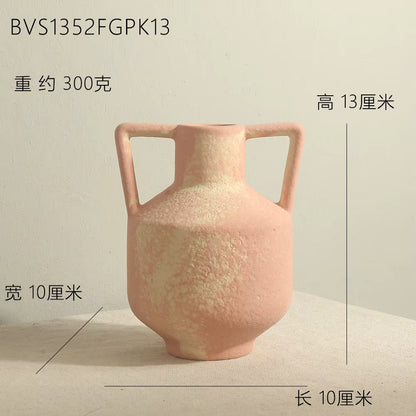 Pink ceramic vase with handles on a beige surface and light gray background