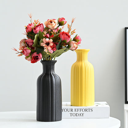Two vases, one black and one yellow, with a bouquet of flowers on a white surface.