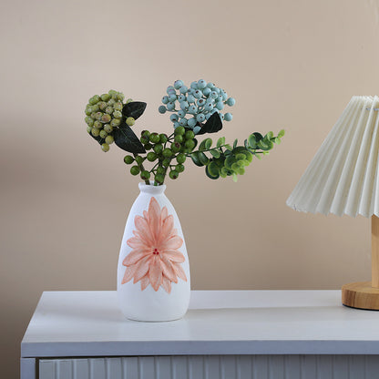 White vase with a pink flower design on a table against a beige wall