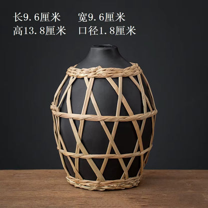 Black vase with woven straw cover on a wooden surface and dark background