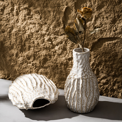 Textured ceramic vase with dried flowers against a textured wall.