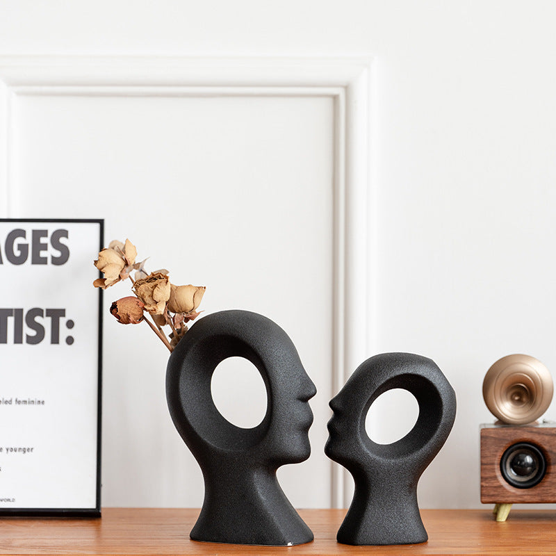Black ceramic head sculptures on a wooden surface with a framed picture and decorative items in the background.