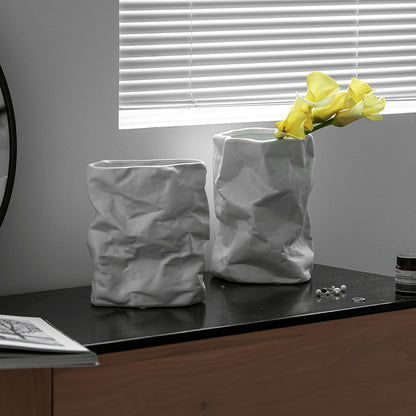 Two textured vases on a surface with one containing yellow flowers.