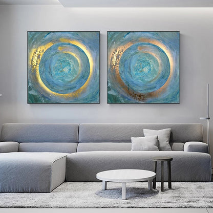Two abstract circular paintings in blue and gold on a wall above a gray sofa.