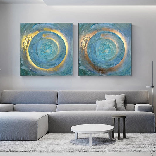 Two abstract circular paintings in blue and gold on a wall above a gray sofa.