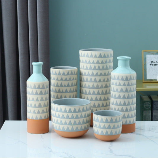 Set of ceramic vases with geometric pattern on a table against a blue wall.