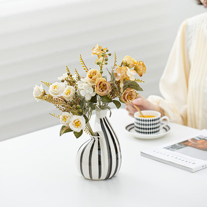 Striped vase with flowers on a table next to a cup of coffee and a book.