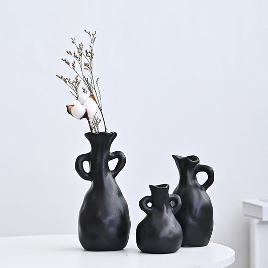 Three black vases of different sizes on a white surface with a light gray background
