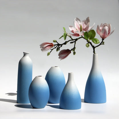 Set of gradient blue vases with a branch of pink flowers on a light gray background
