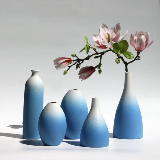 Set of gradient blue vases with a branch of pink flowers on a light gray background