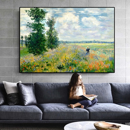 Woman reading a book on a gray sofa with a large framed painting of a landscape above her.