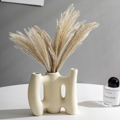 Ceramic vase with dried plants on a white surface with a gray background