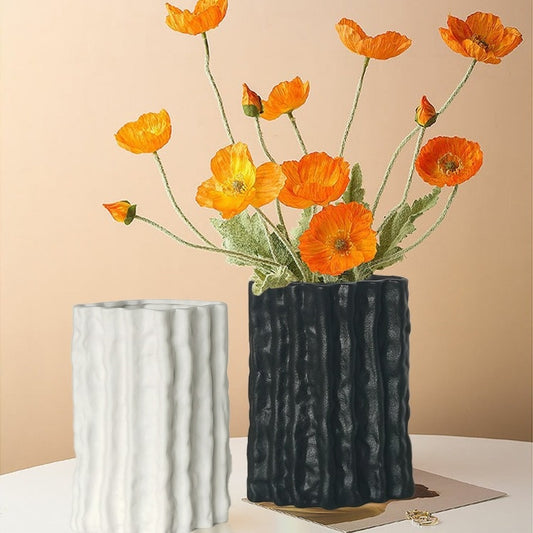 Two textured vases, one black and one white, with orange flowers on a beige background.