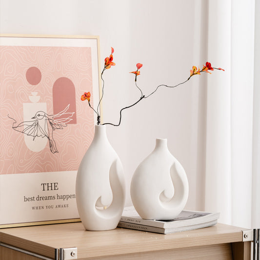 Two white vases with floral branches on a wooden surface with a pink poster in the background.