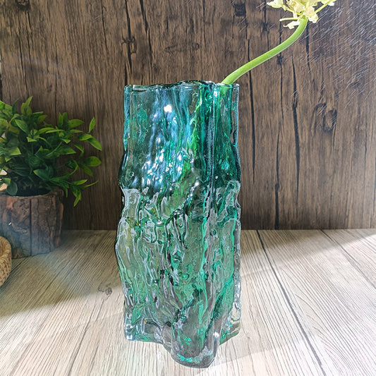 Green textured glass vase on a wooden surface with a wooden wall background