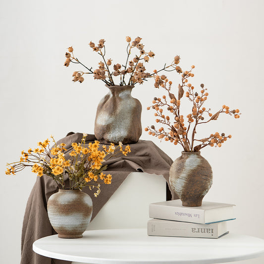 Three ceramic vases with dried flowers on a white surface
