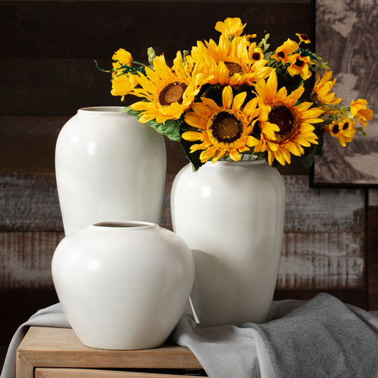 Three white vases with a bouquet of sunflowers on a wooden surface.