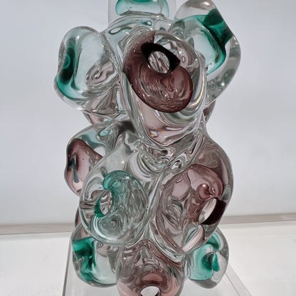 Glass sculpture with swirls of green, pink, and clear on a white background