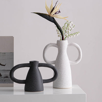 Two ceramic vases, one black and one white with handles, on a light surface with a neutral background.