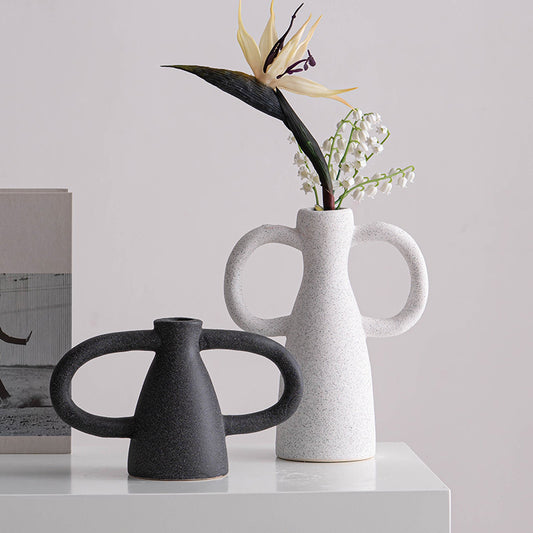 Two ceramic vases, one black and one white with handles, on a light surface with a neutral background.