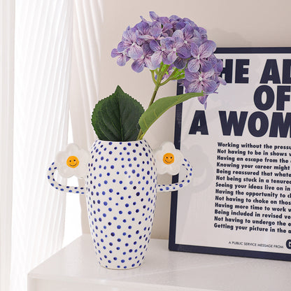 Polka dot vase with purple flowers on a shelf next to a framed text poster.