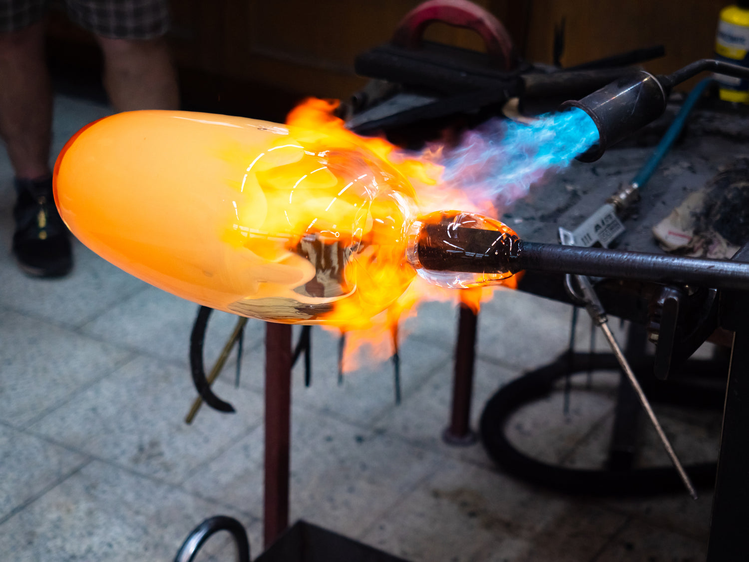 Glassblowing process with a glowing glass object and flame in a workshop setting.